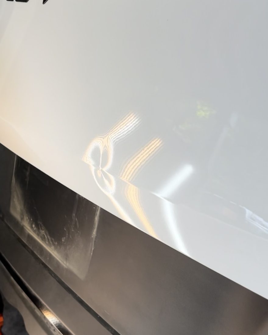 Before: the striped light bends over a dent in the white hatch of a Kia Sportage
