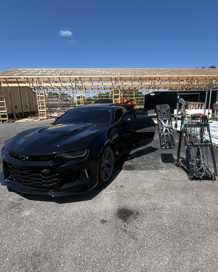 A black Camaro parked at a construction site with a dent light beside it