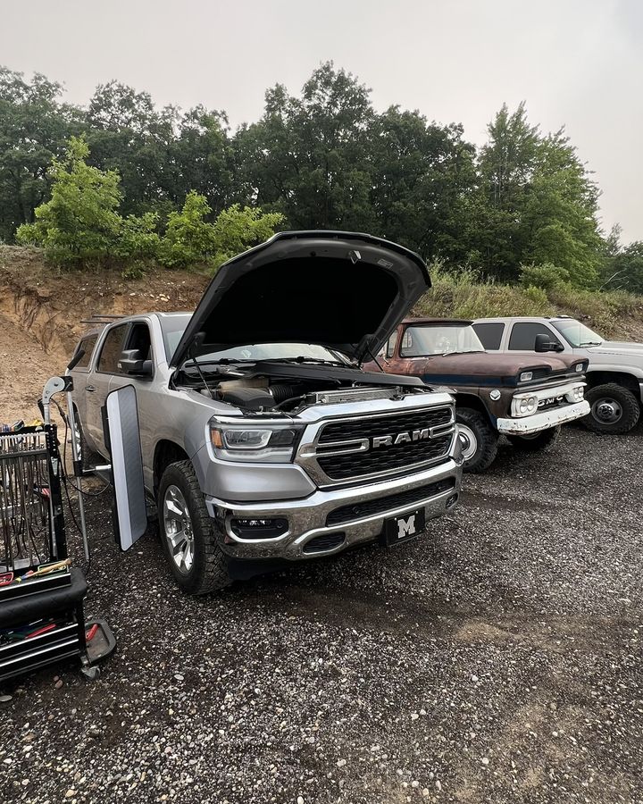 A white Ram pickup with the hood up at a gravel pit