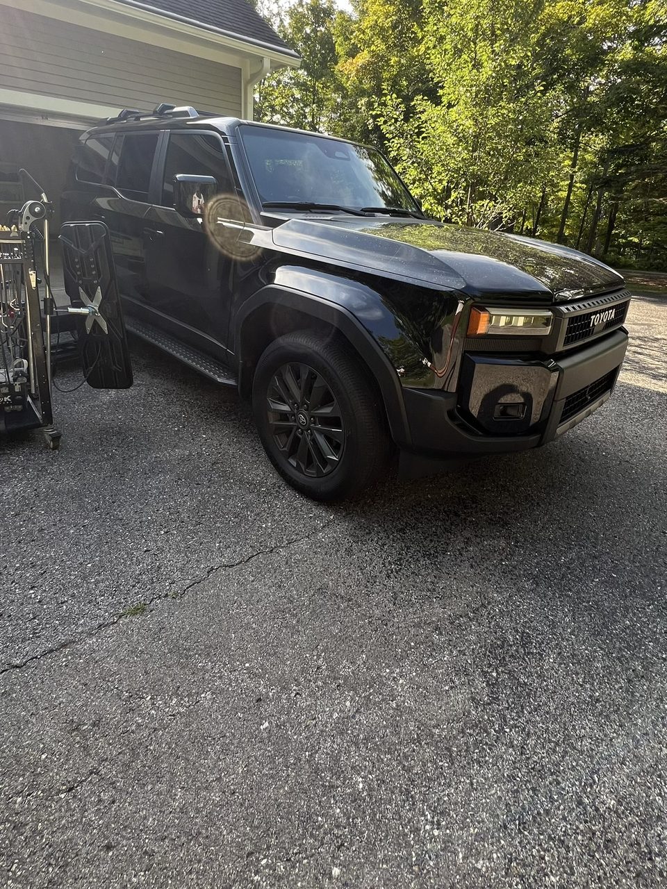 A black Toyota Land Cruiser parked in a driveway, with a dent light and tool cart set up beside it