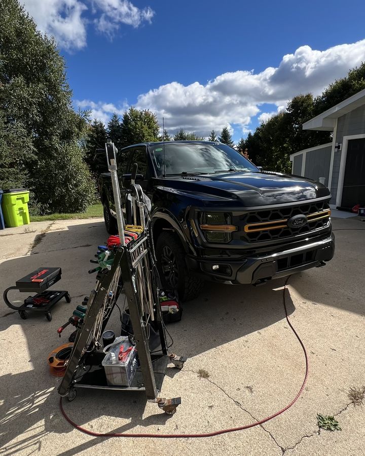 A black Ram pickup in a driveway with a dent light and tool cart set up beside it