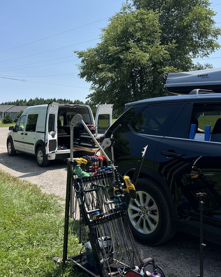 A van and tool cart parked on a gravel driveway beside a black SUV