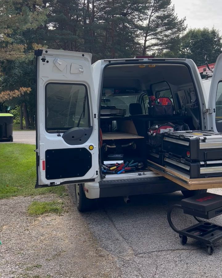Ethan's van with the back doors open and tool drawers pulled out, parked under pine trees